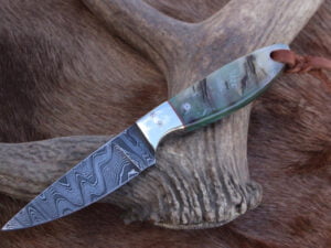 Damascus cowboy knife with distinct blade pattern, full tang construction, and ram horn handle. Leather sheath included.