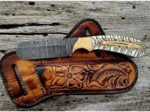 Handcrafted Damascus Cowboy Bull Cutter Knife with intricate Damascus steel blade pattern, brass bolsters, and pine cone handle, displayed alongside its cowhide leather sheath