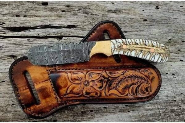 Handcrafted Damascus Cowboy Bull Cutter Knife with intricate Damascus steel blade pattern, brass bolsters, and pine cone handle, displayed alongside its cowhide leather sheath