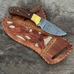 Damascus Cowboy Knife With Leather Sheath - A beautifully crafted knife showcasing a stunning twist pattern on the blade and a natural rosewood handle, resting on its handmade cowhide leather sheath.