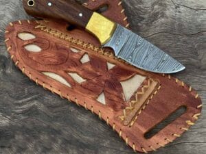 Damascus Cowboy Knife With Leather Sheath - A beautifully crafted knife showcasing a stunning twist pattern on the blade and a natural rosewood handle, resting on its handmade cowhide leather sheath.